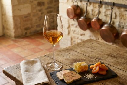 Accord sucré-salé avec un verre de Sauternes doré accompagné de foie gras, miel en rayon et abricots secs sur une ardoise en cuisine rustique française